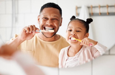 Hygiène Bucco-Dentaire Chez Les Tout-Petits Happy mixed race father and daughter brushing their teeth together in a bathroom at home. Single African American parent teaching his daughter to protect her teeth