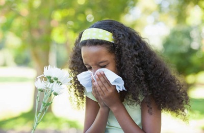 Young girl sitting by flower and blowing her nose in the park on a sunny day